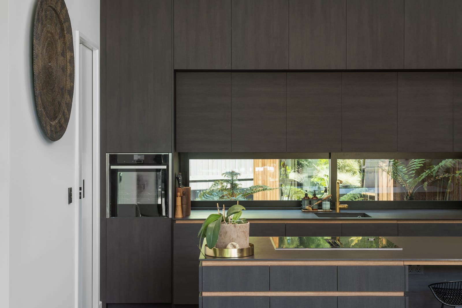 David Street kitchen, dark timber cabinetry with brass tapware and bush outlook