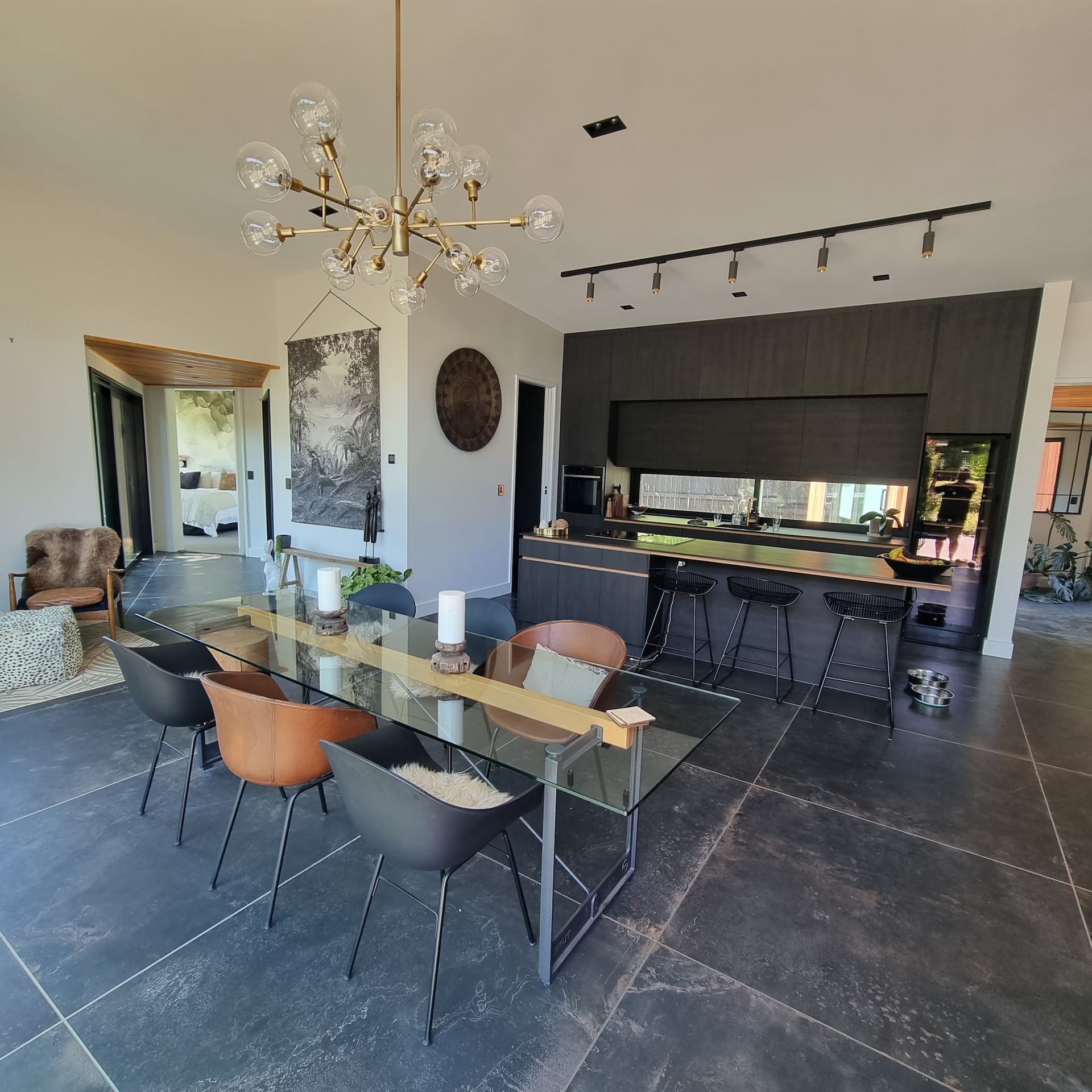 Open plan dining and kitchen with dark cabinetry and brass chandelier